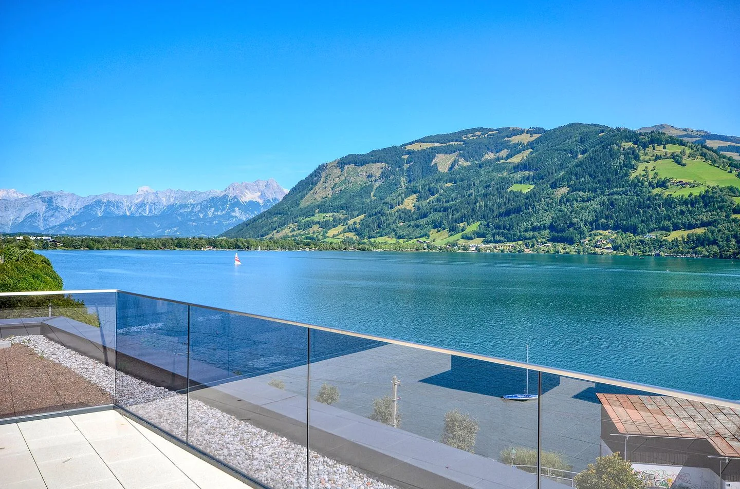 Una terraza junto al lago con barandilla de vidrio mira al agua y a montañas verdes.