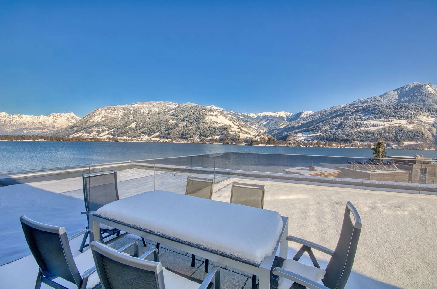 Una zona de comedor al aire libre da a un lago y montañas nevadas.