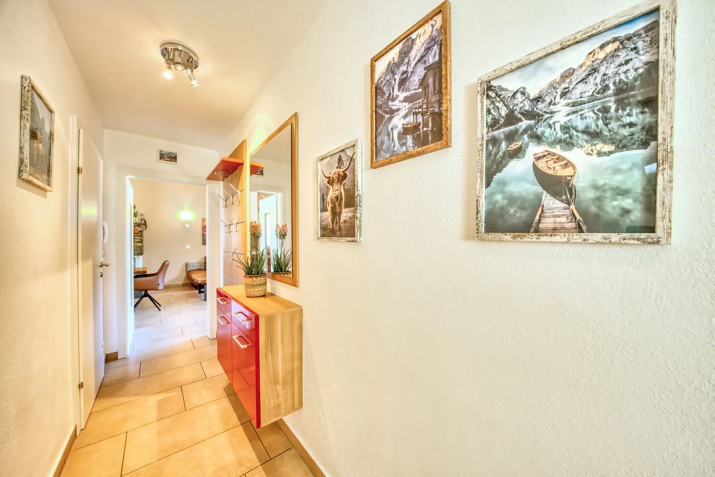 A bright hallway with framed landscape pictures and a red storage cabinet.