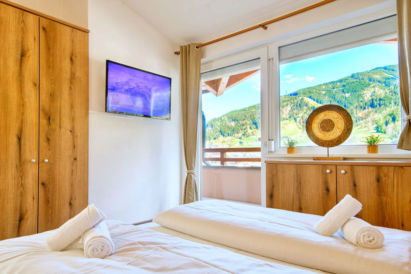 A bedroom with white bedding, wooden wardrobes, and windows overlooking green hills.