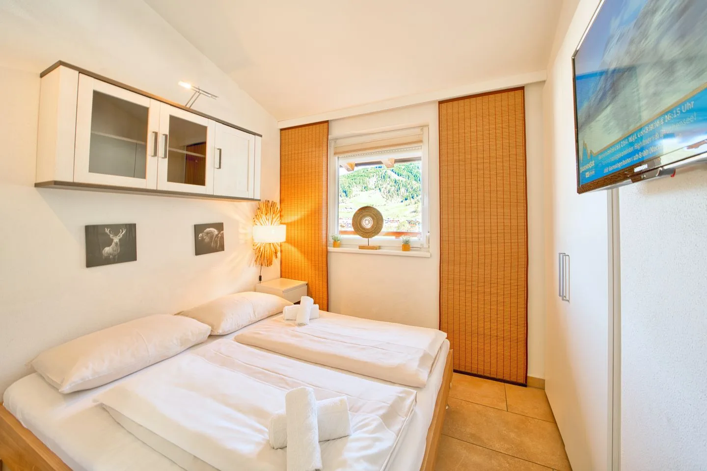 A bedroom with white bedding, built-in cabinets, and a window.