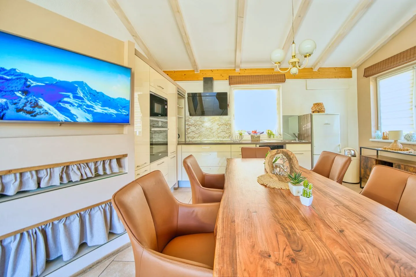 A dining area with a long wooden table and a kitchen in the background.