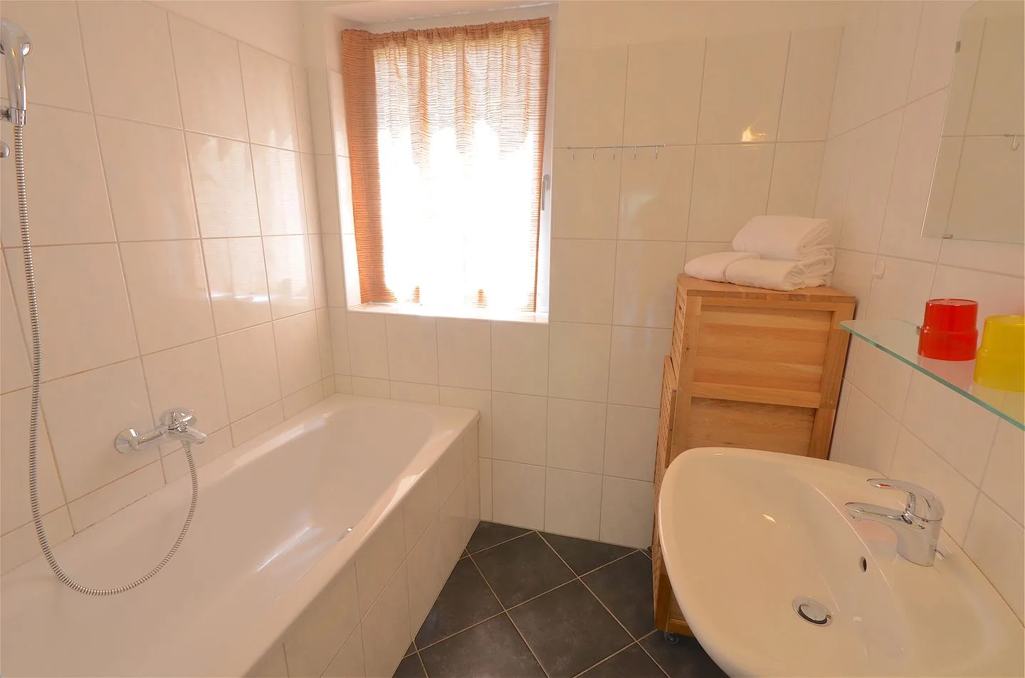 Un baño con azulejos, bañera, lavabo y una ventana luminosa.