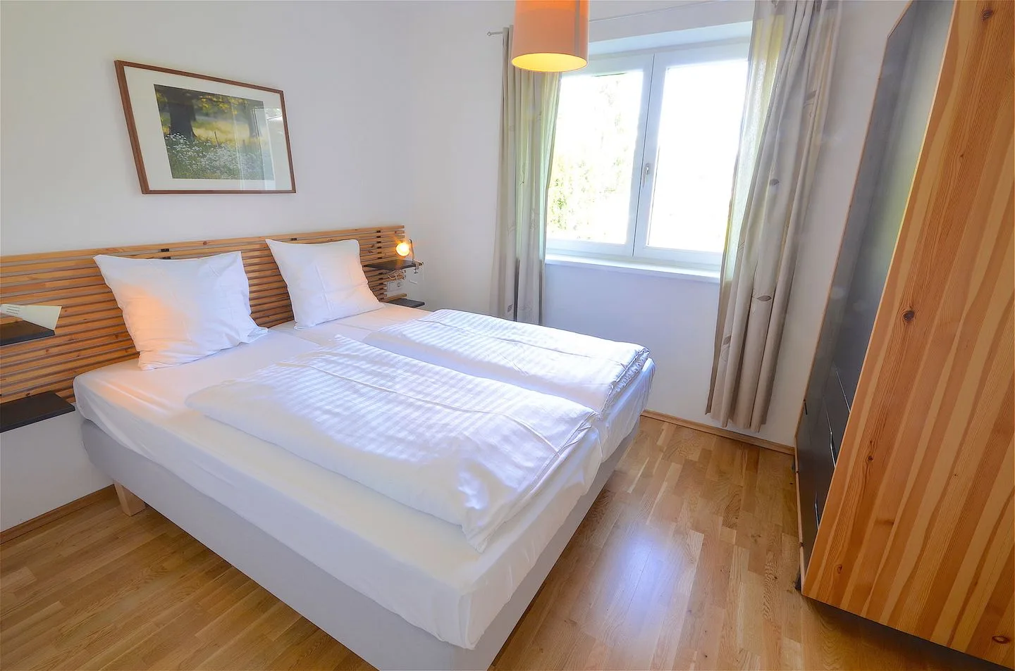 Un dormitorio luminoso con una cama bien tendida y una ventana grande.