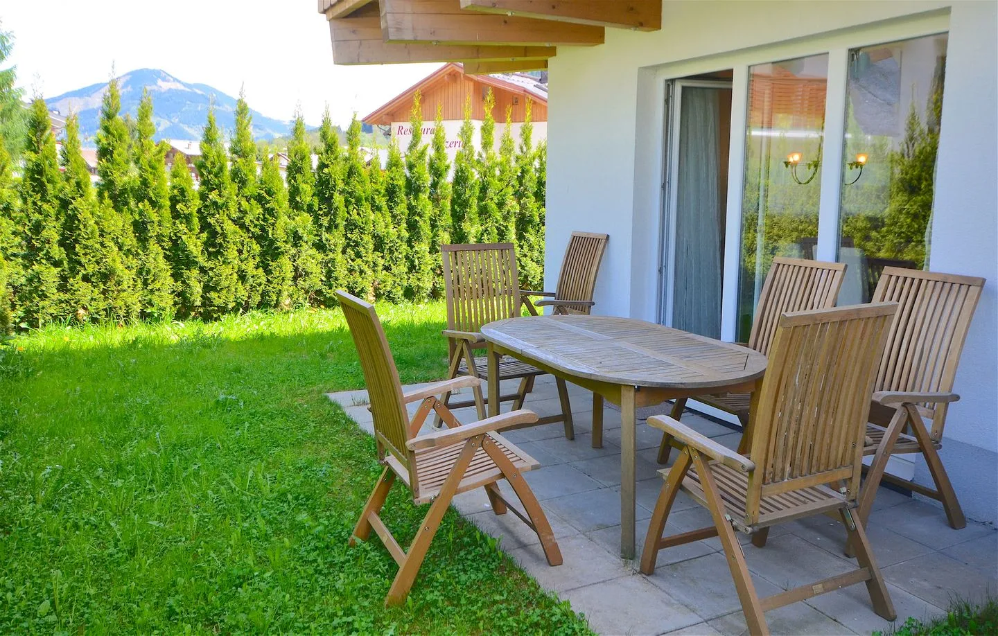 Un patio exterior con una mesa y sillas de madera junto a un jardín con césped.