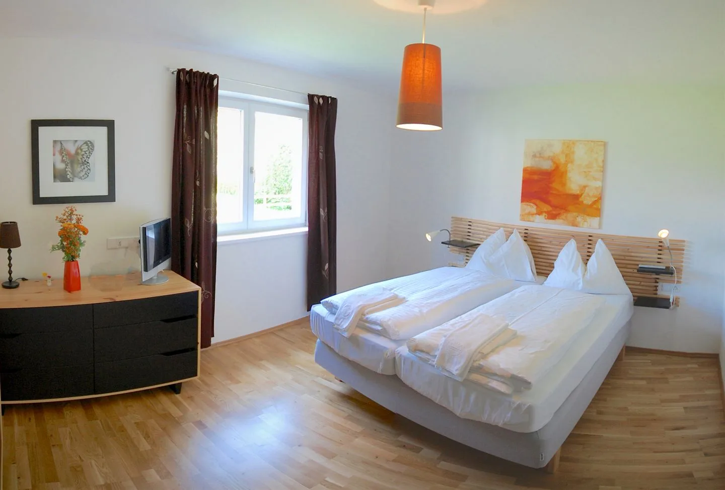 Un dormitorio luminoso con dos camas, una ventana y suelo de madera cálida.