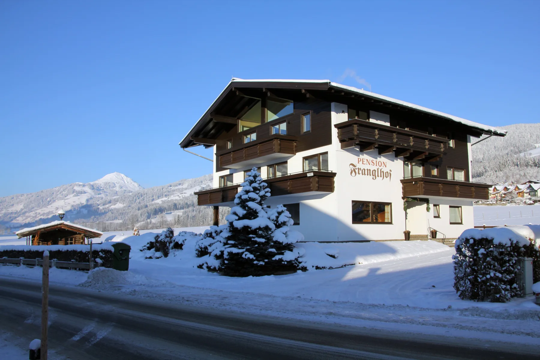 Zona común: Un edificio de pensión está junto a una carretera nevada, con montañas al fondo.