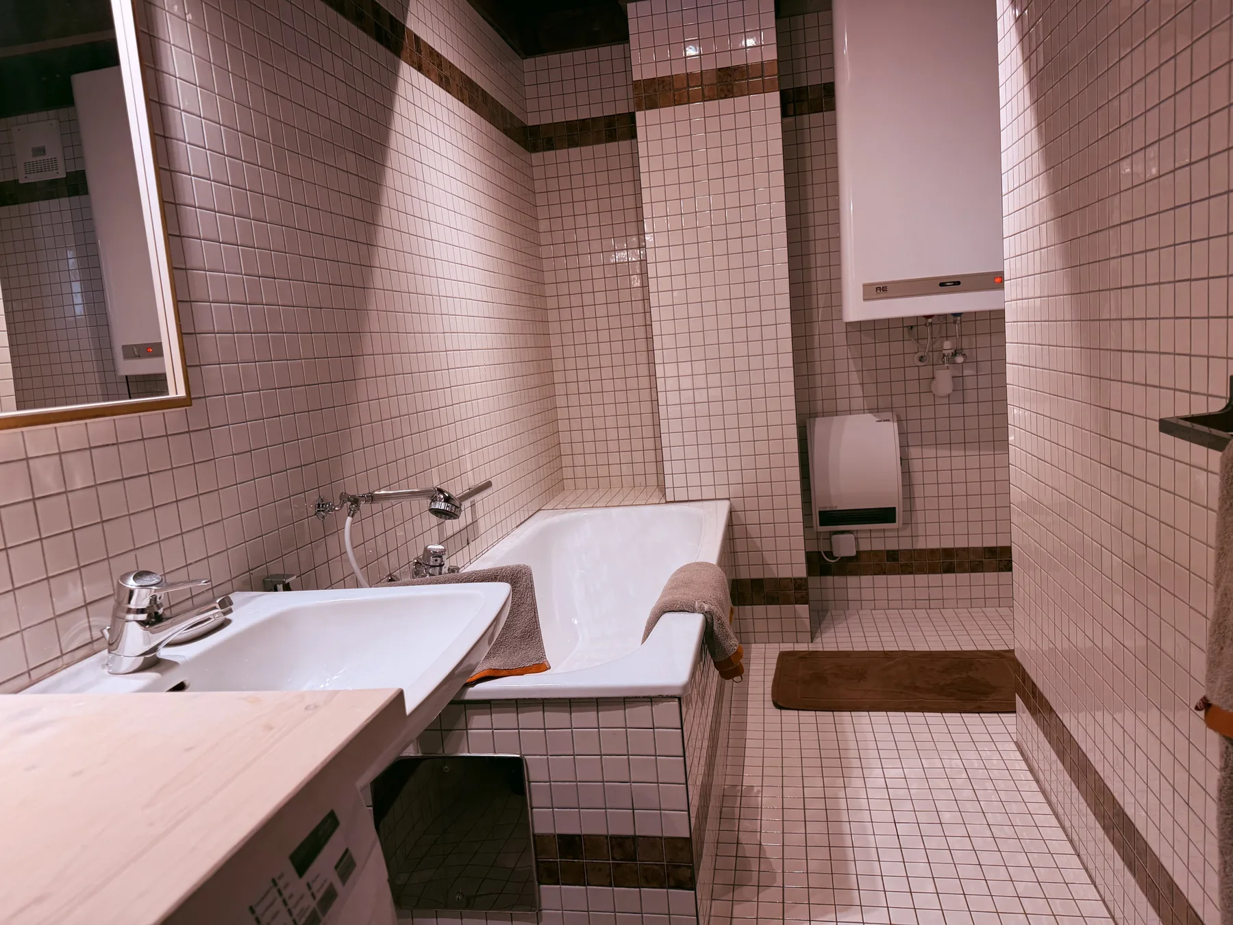 A tiled bathroom with a bathtub, sink, and wall-mounted fixtures.