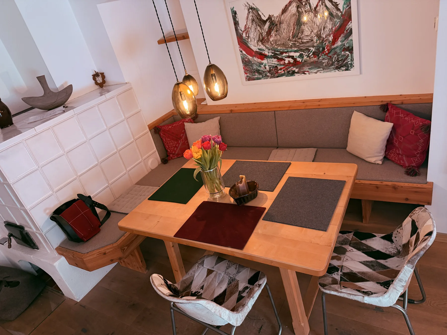 A dining nook with a wooden table, cushioned seating, and pendant lights.