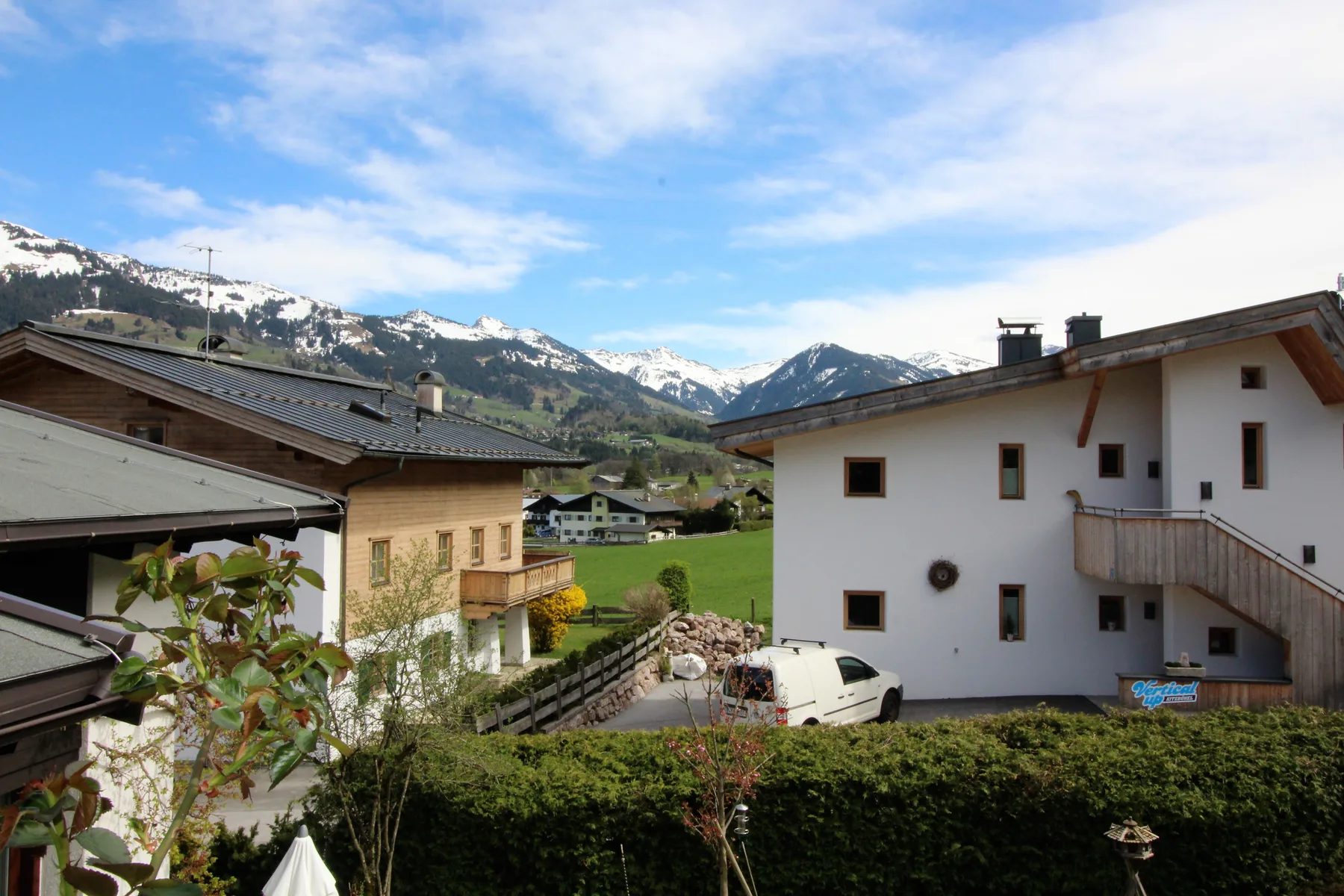 Mountain village buildings overlook a green valley beneath snow-capped peaks.