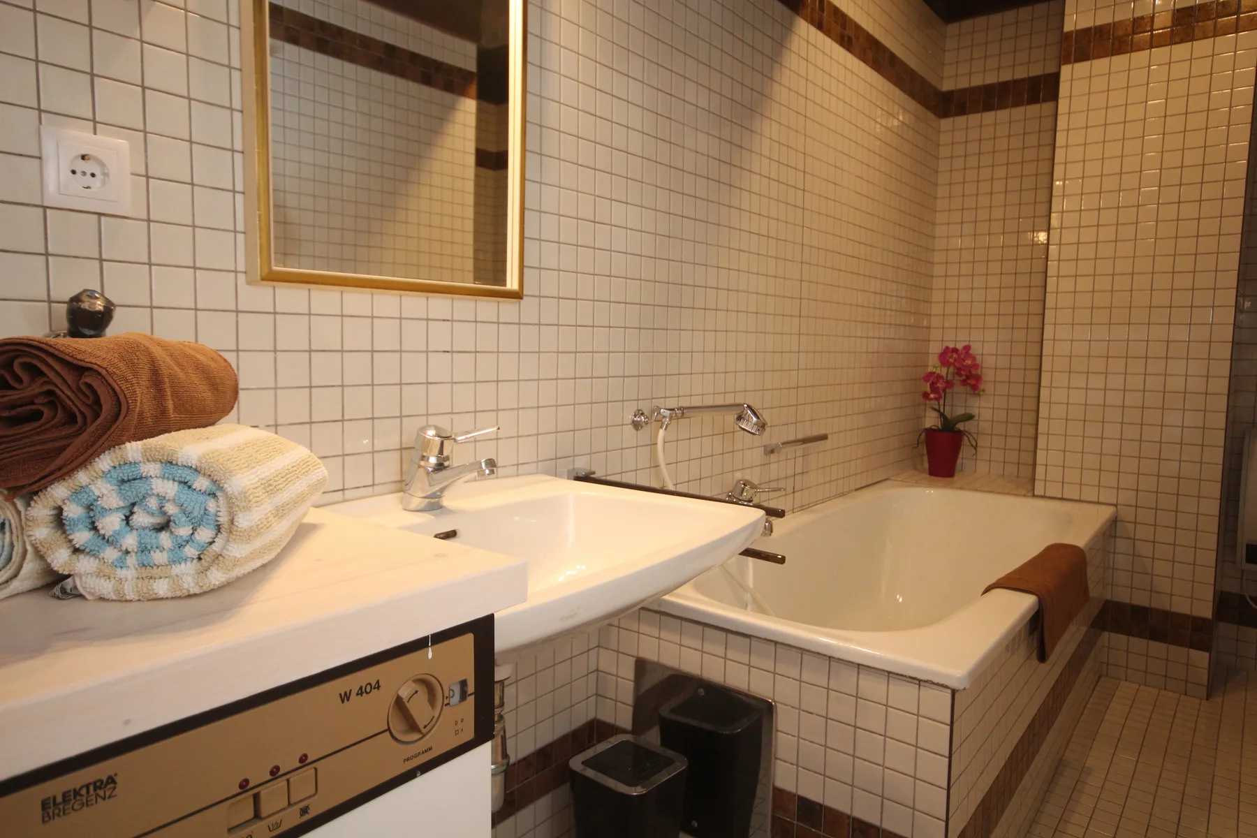 A tiled bathroom with a sink, bathtub, and folded towels.