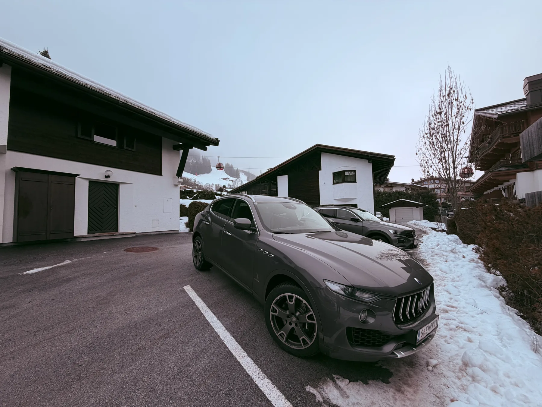 Shared amenity: A gray car is parked outside dark-trimmed buildings beside snow.