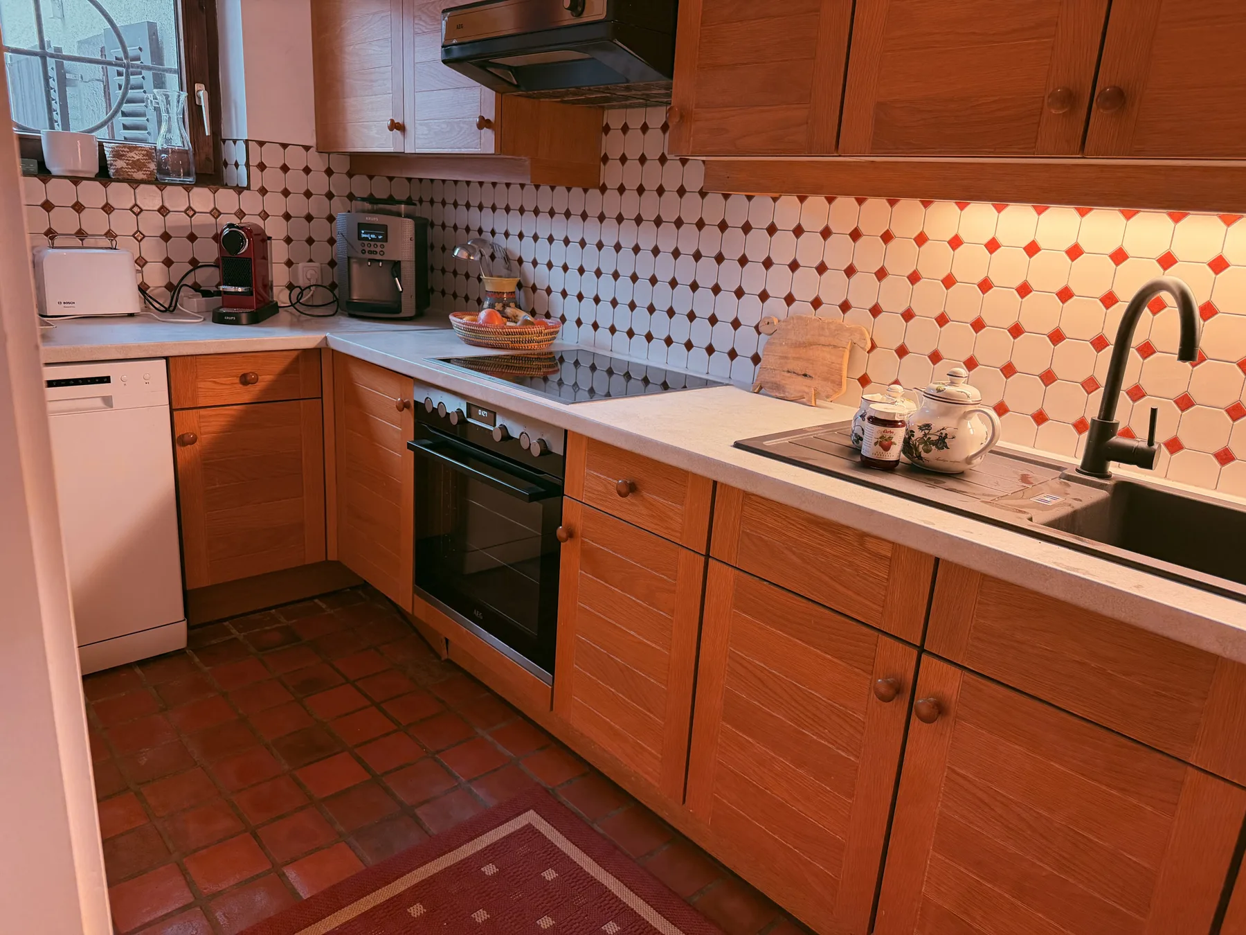 A kitchen with wooden cabinets, tiled walls, and a long countertop.
