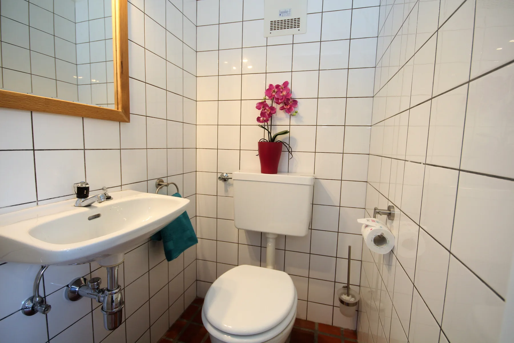 A tiled bathroom with a sink, toilet, and potted orchid.