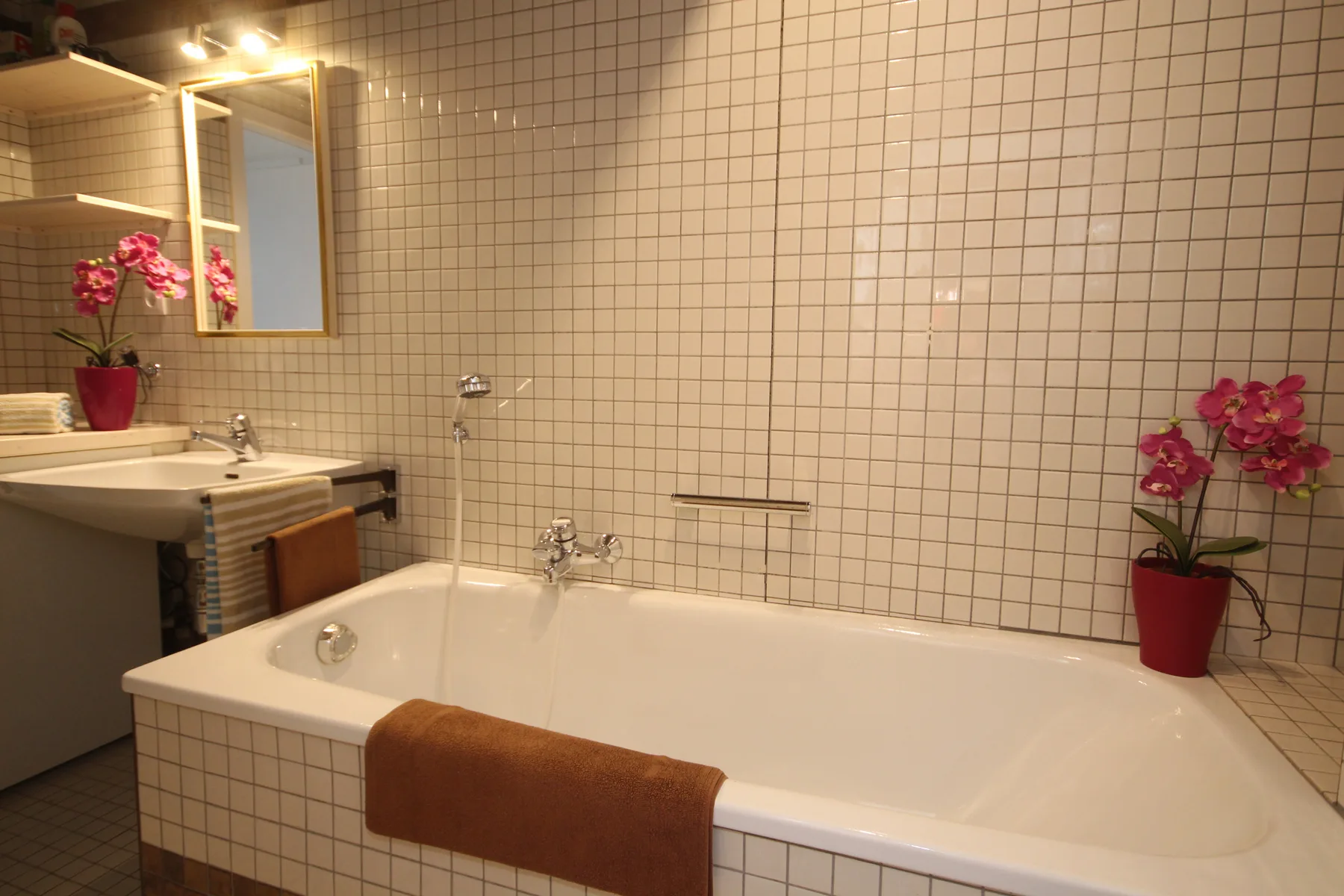 A tiled bathroom with a bathtub, sink, and potted orchids.