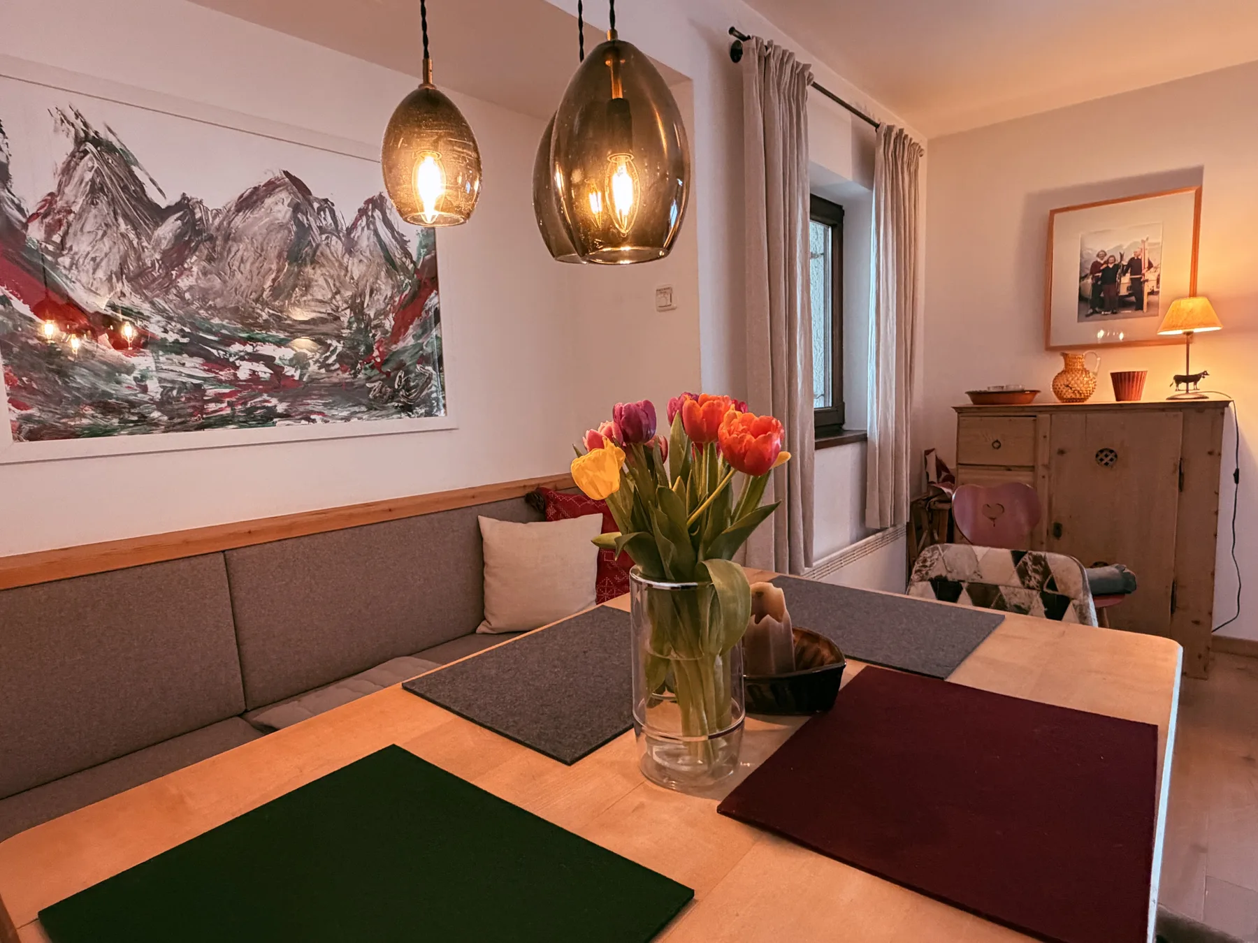 A dining and seating area features a table with flowers and a mountain painting.