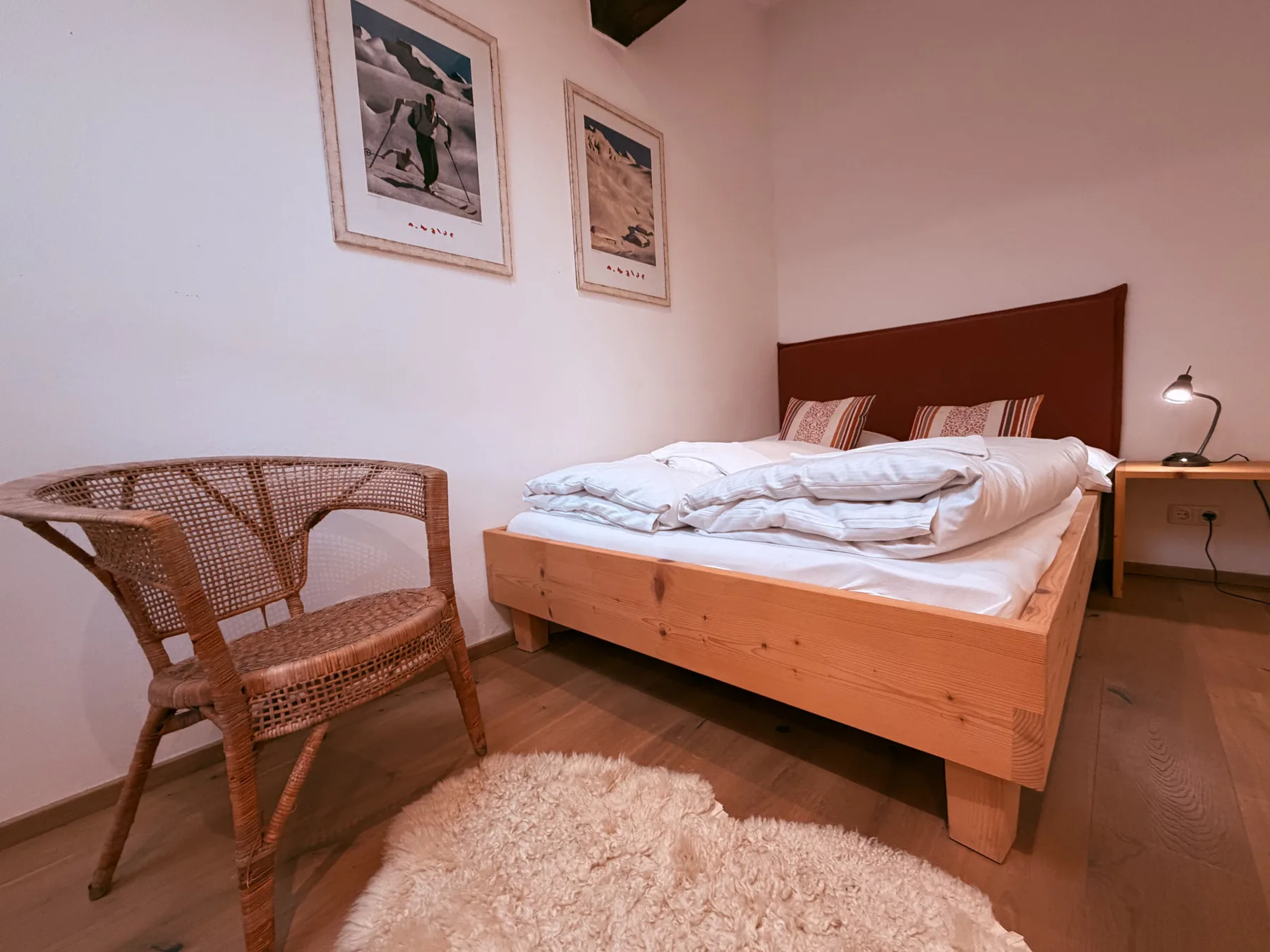 A bedroom with a wooden bed, folded bedding, and a woven chair.