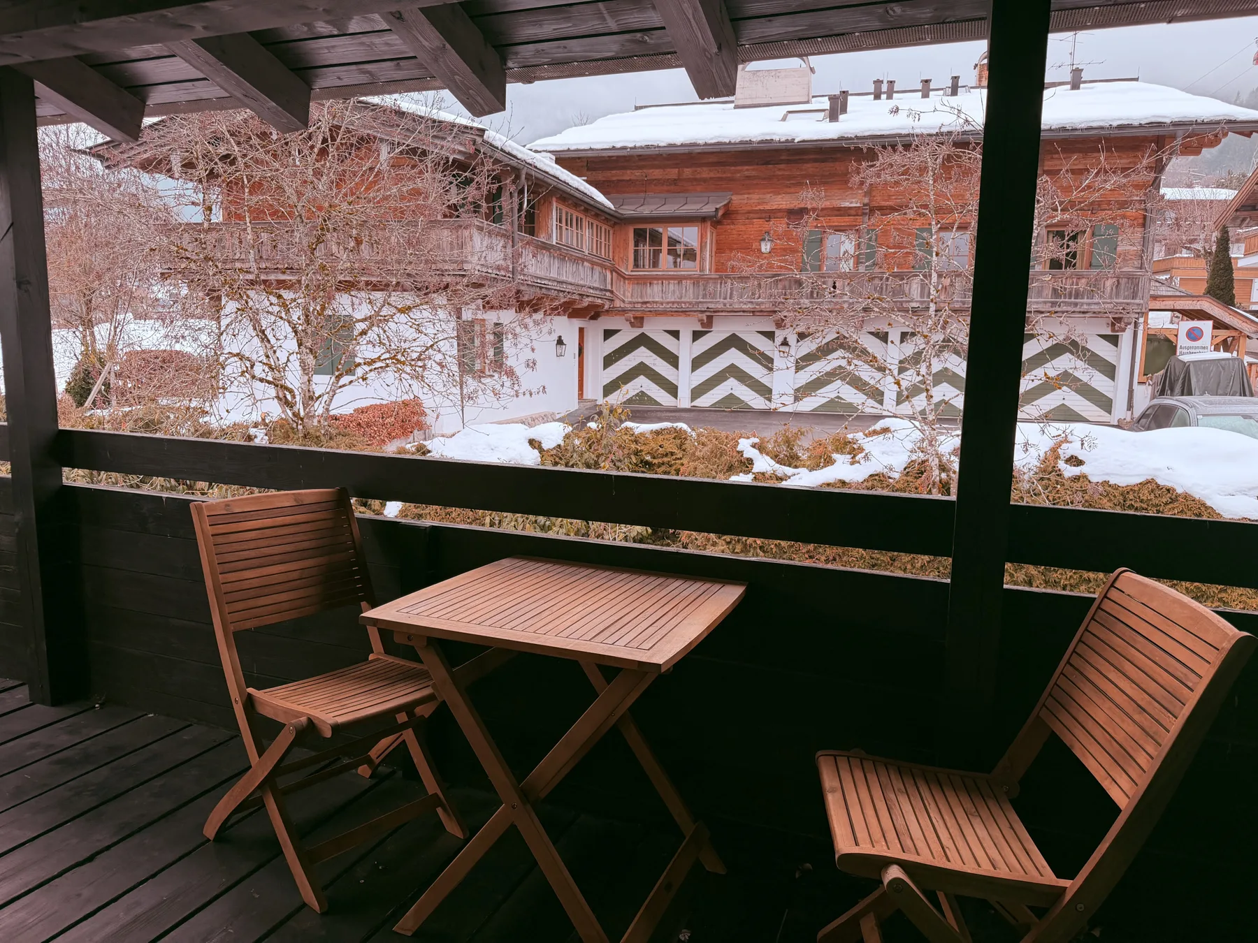 A covered wooden balcony with seating overlooks snow-covered buildings and trees.