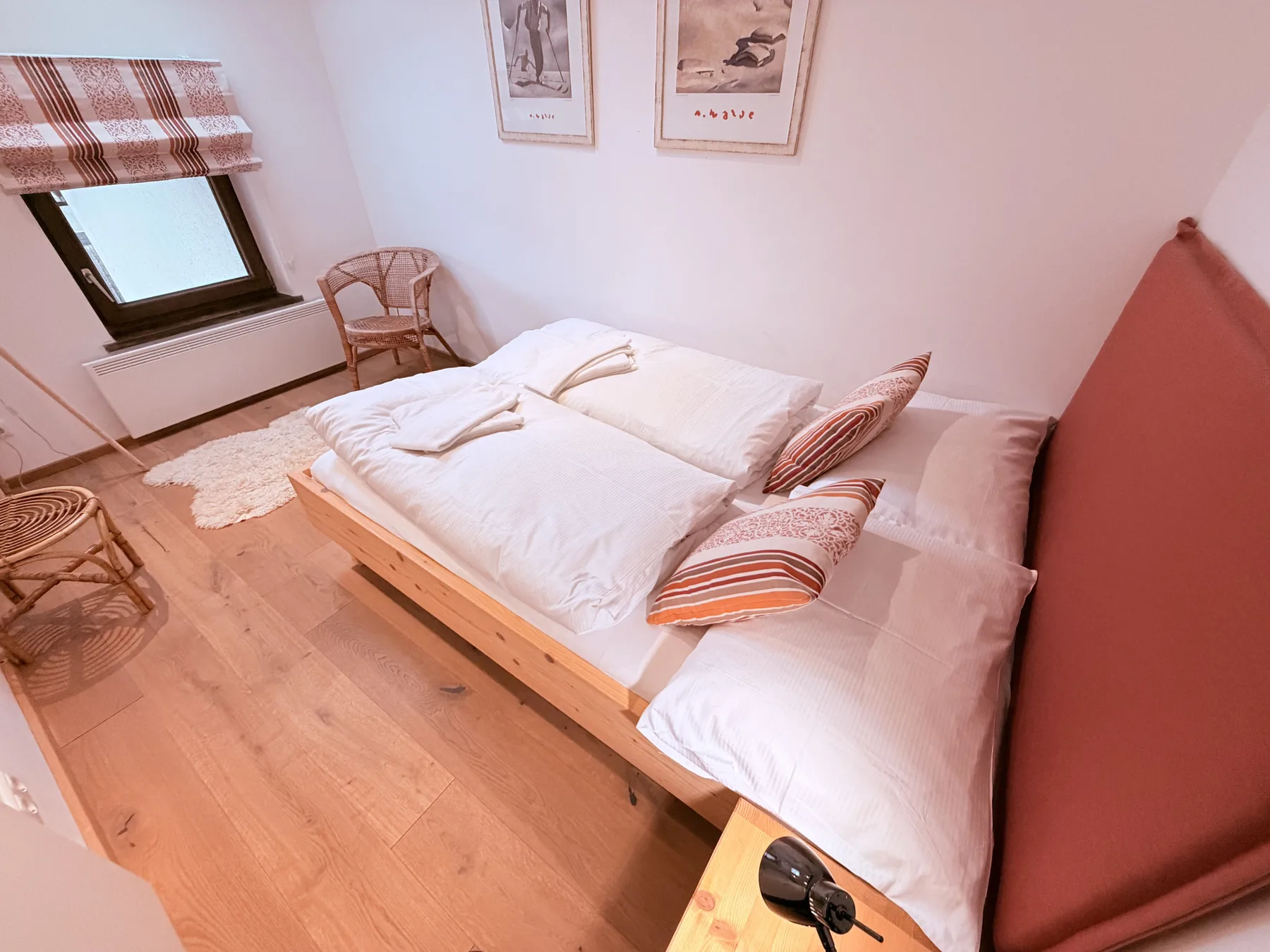A bedroom with a low bed, white bedding, and framed prints above it.