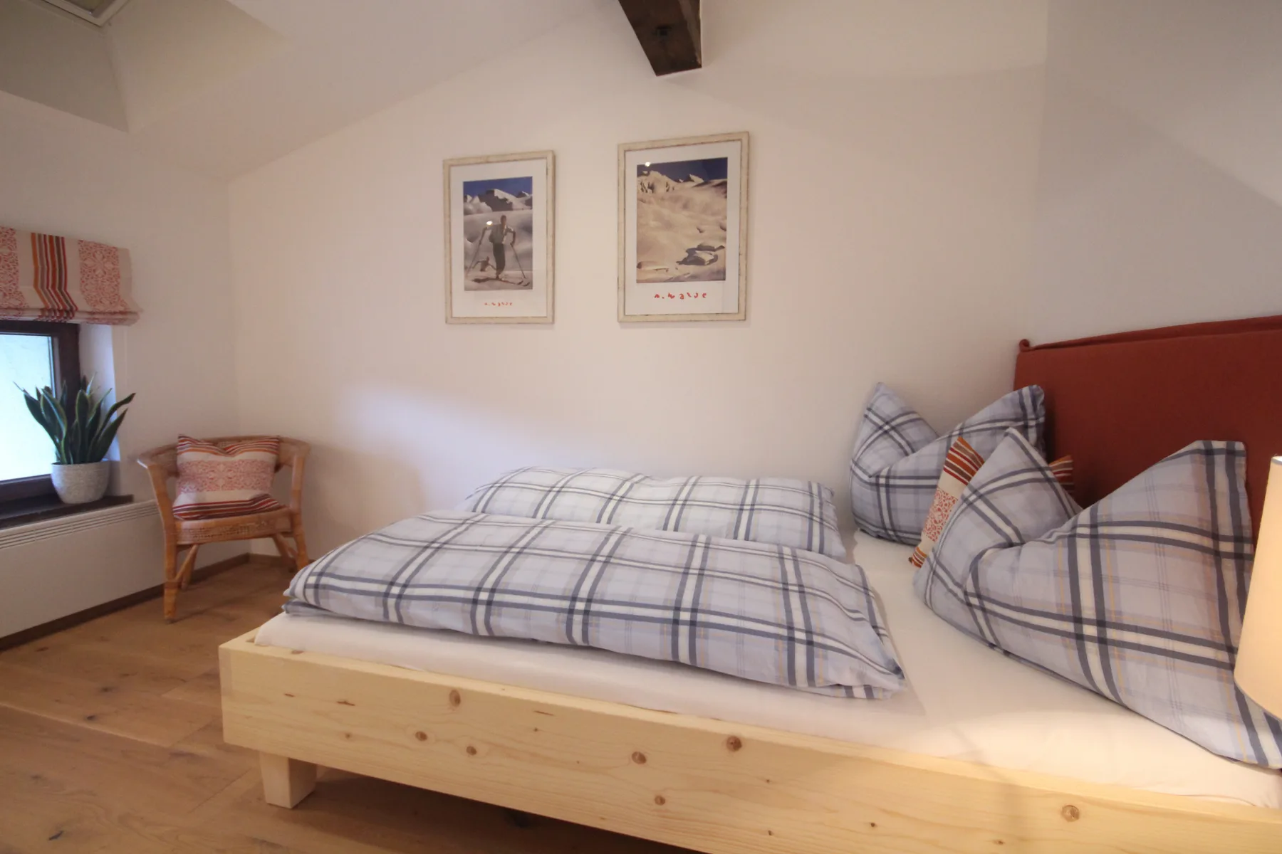 A bedroom with a wooden bed dressed in plaid bedding and a chair by the window.