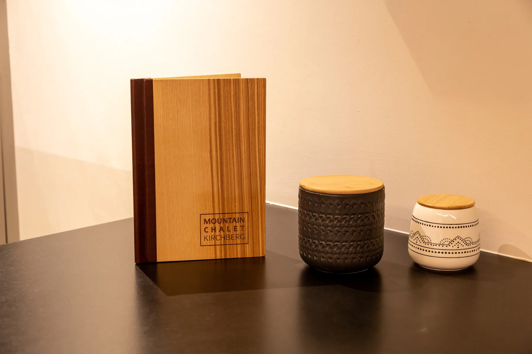 A tabletop displays a wooden menu, a dark patterned container, and a small decorated jar.