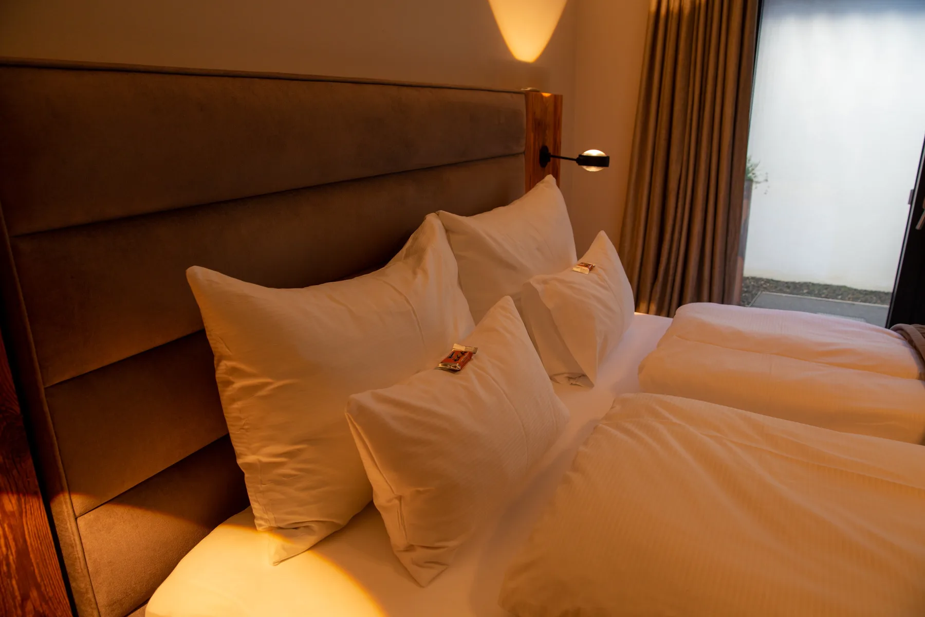A bedroom with white bedding and pillows beside a curtained window.