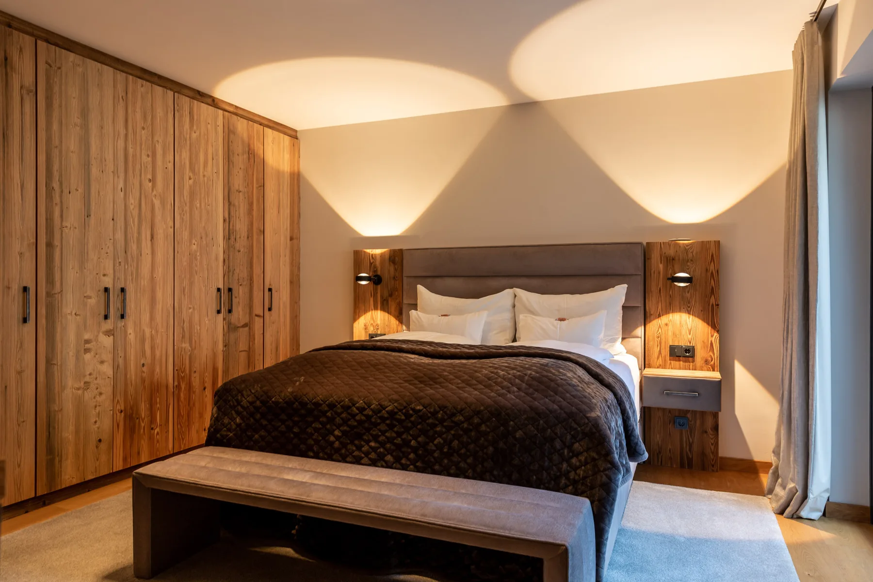 A bedroom with a double bed, wooden wardrobes, and a bench at the foot of the bed.