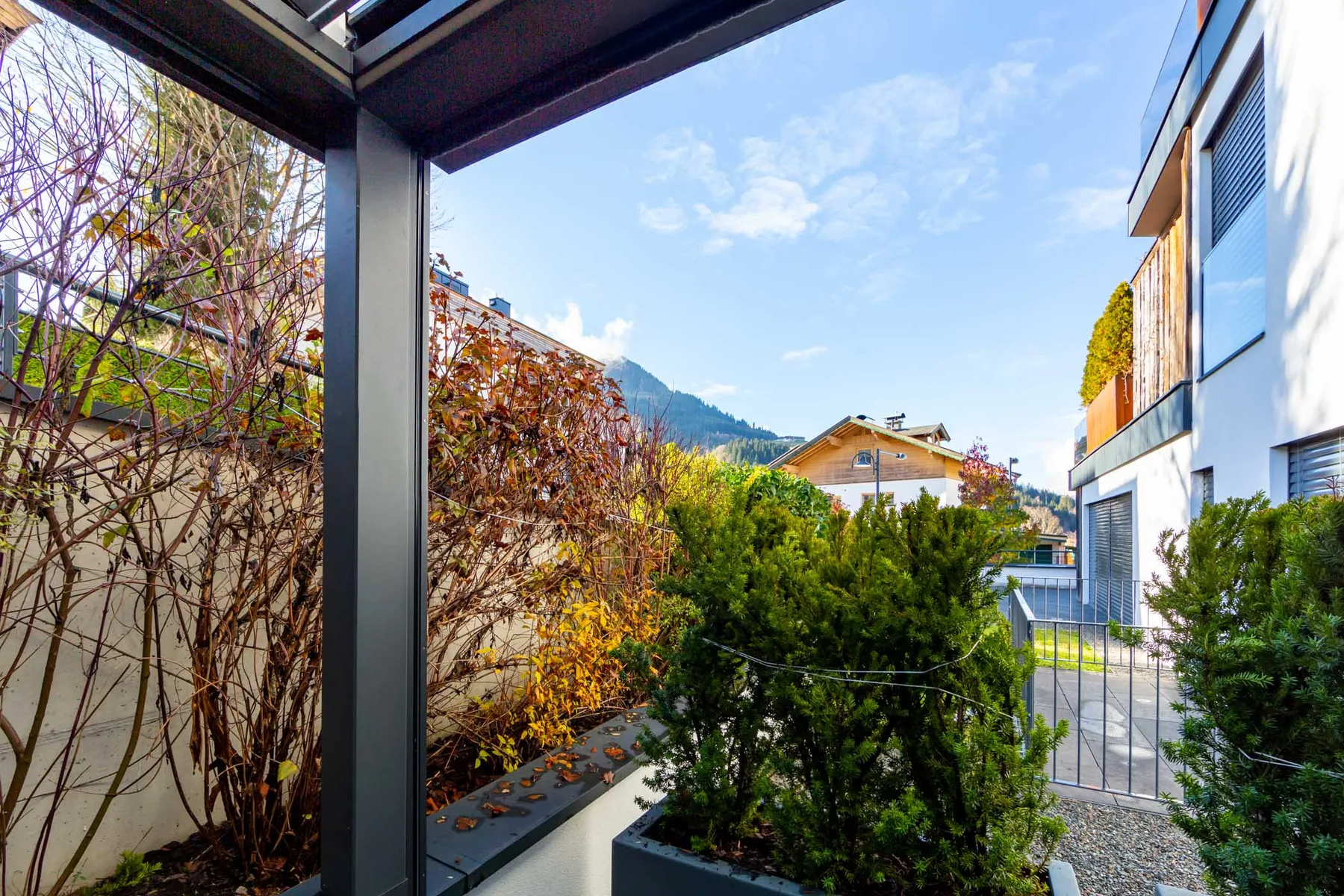A garden courtyard with shrubs, neighboring buildings, and distant mountains under a blue sky.