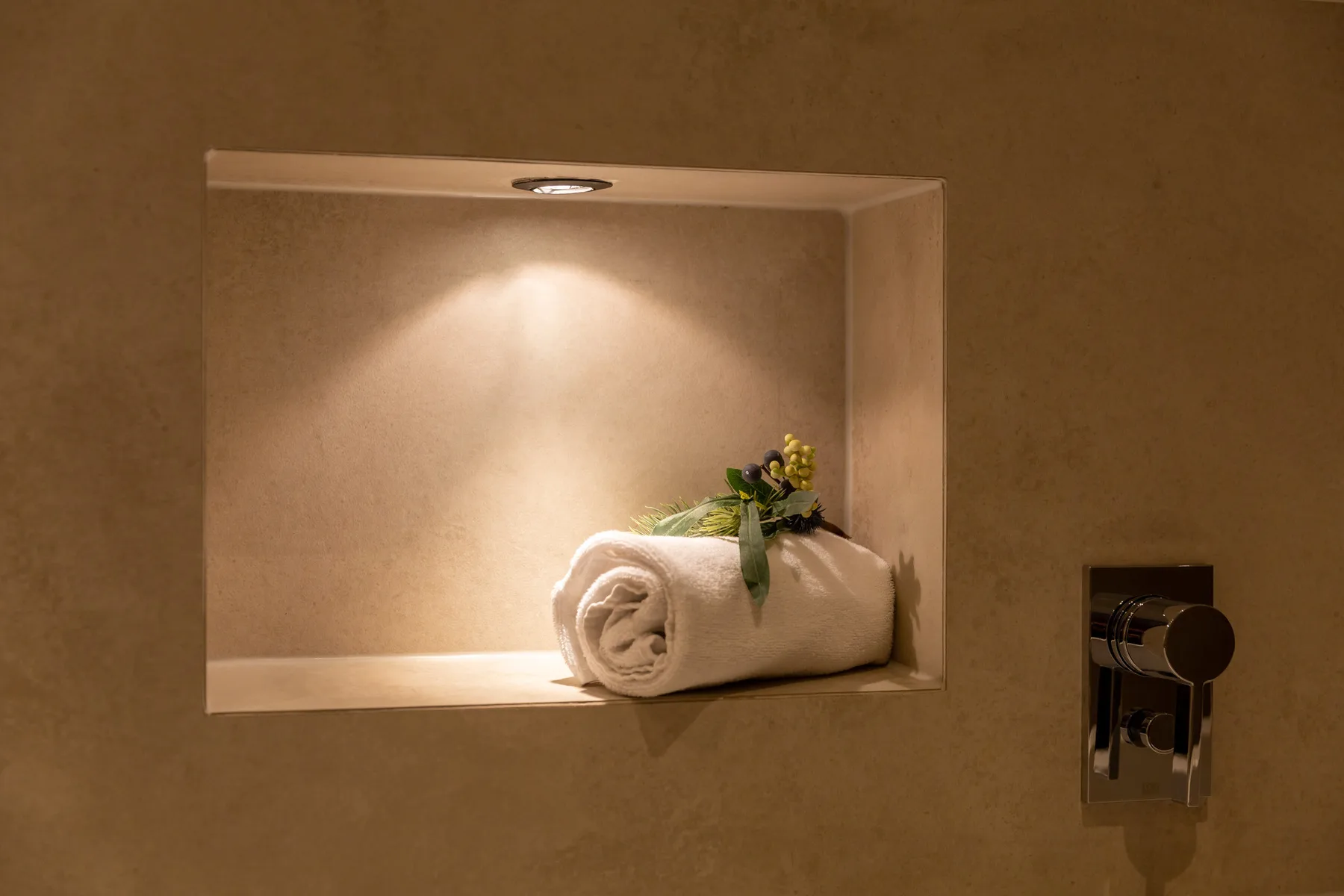 A recessed wall niche holds a rolled white towel and a small floral arrangement.