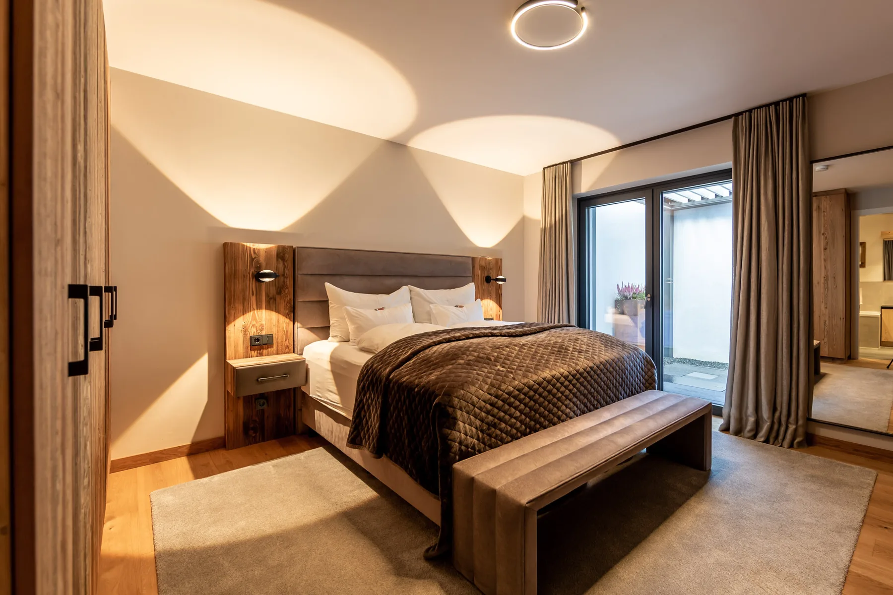 A bedroom with a bed, a bench, and sliding glass doors.