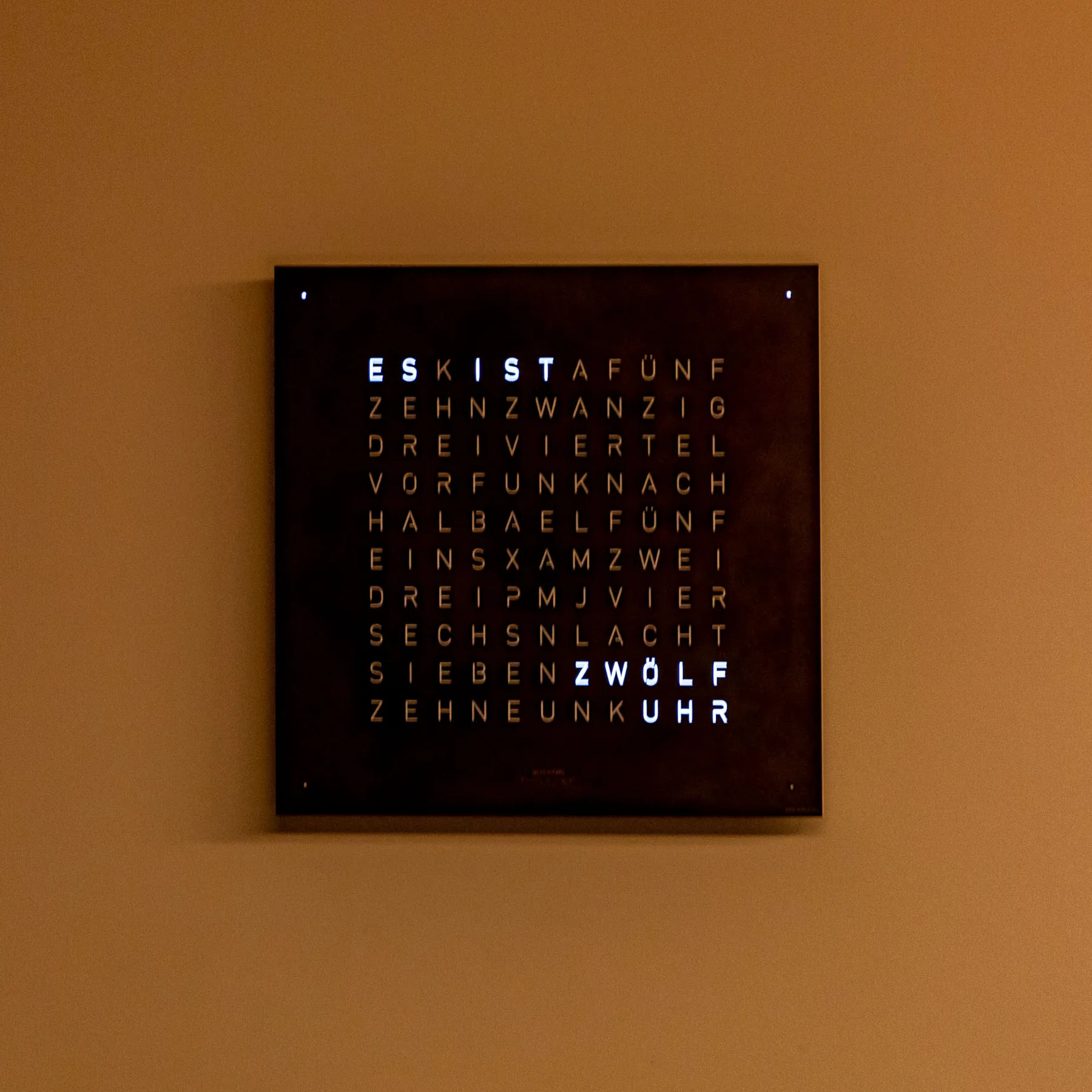 A framed word-art display hangs on a plain tan wall.