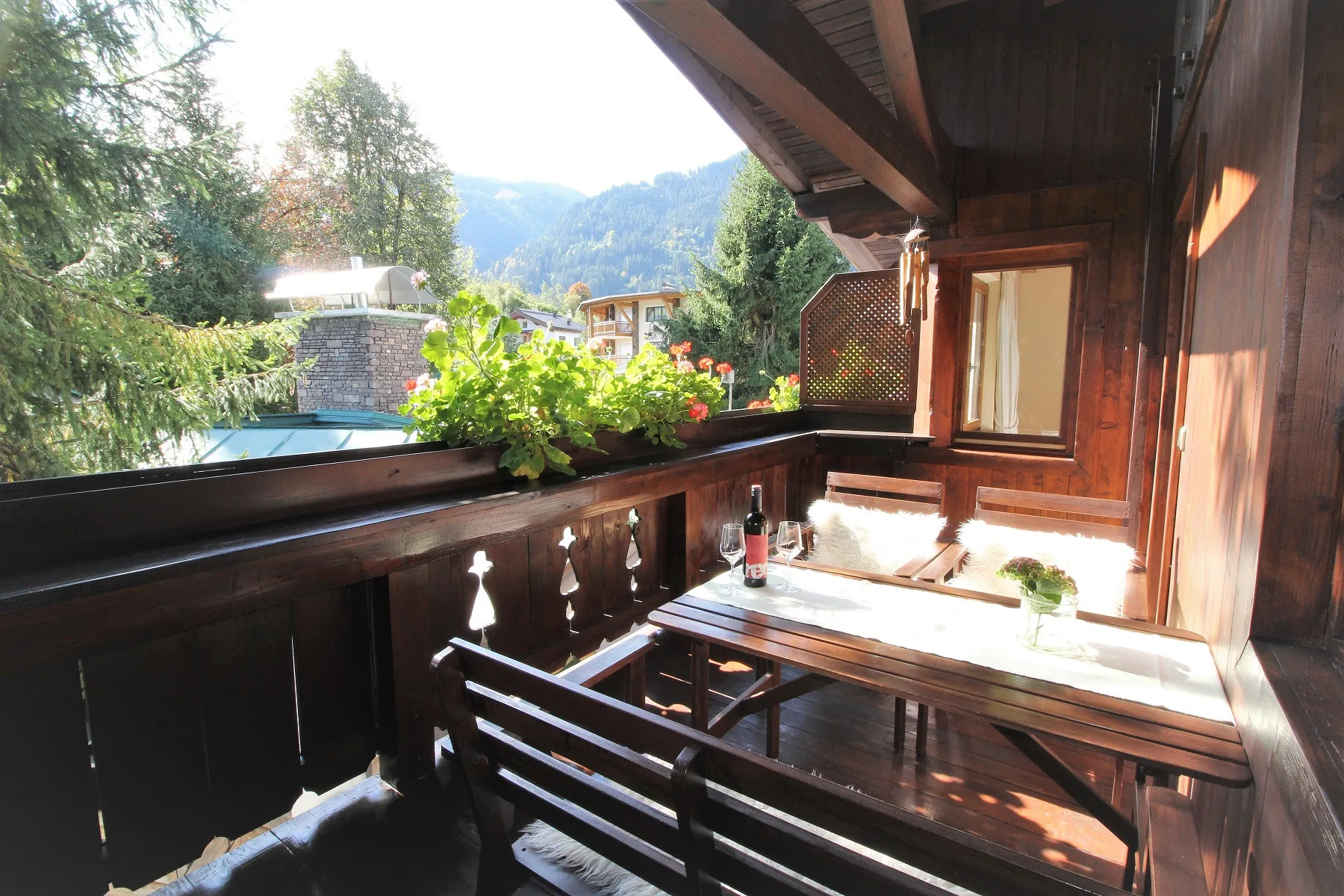 A wooden balcony with outdoor seating overlooks trees and a mountain view.