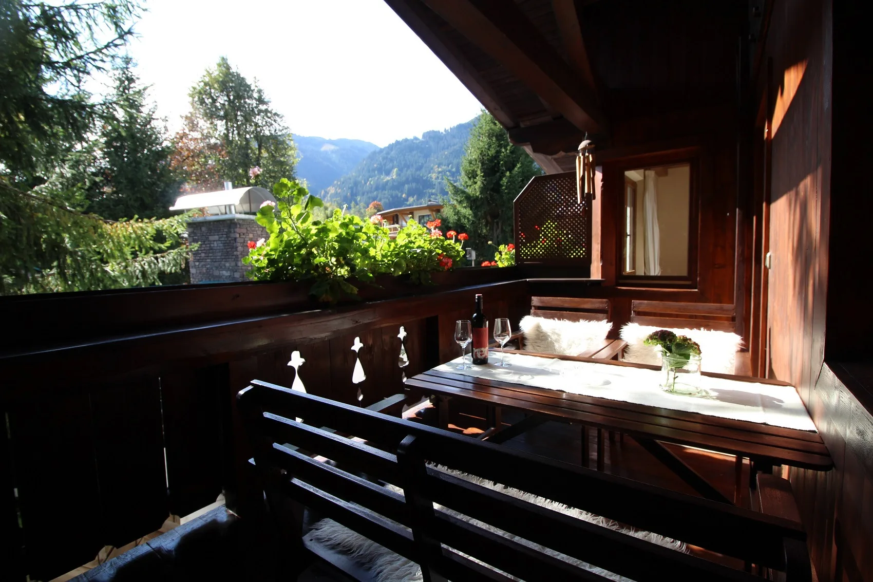 A covered wooden balcony with a table overlooks greenery and distant mountains.
