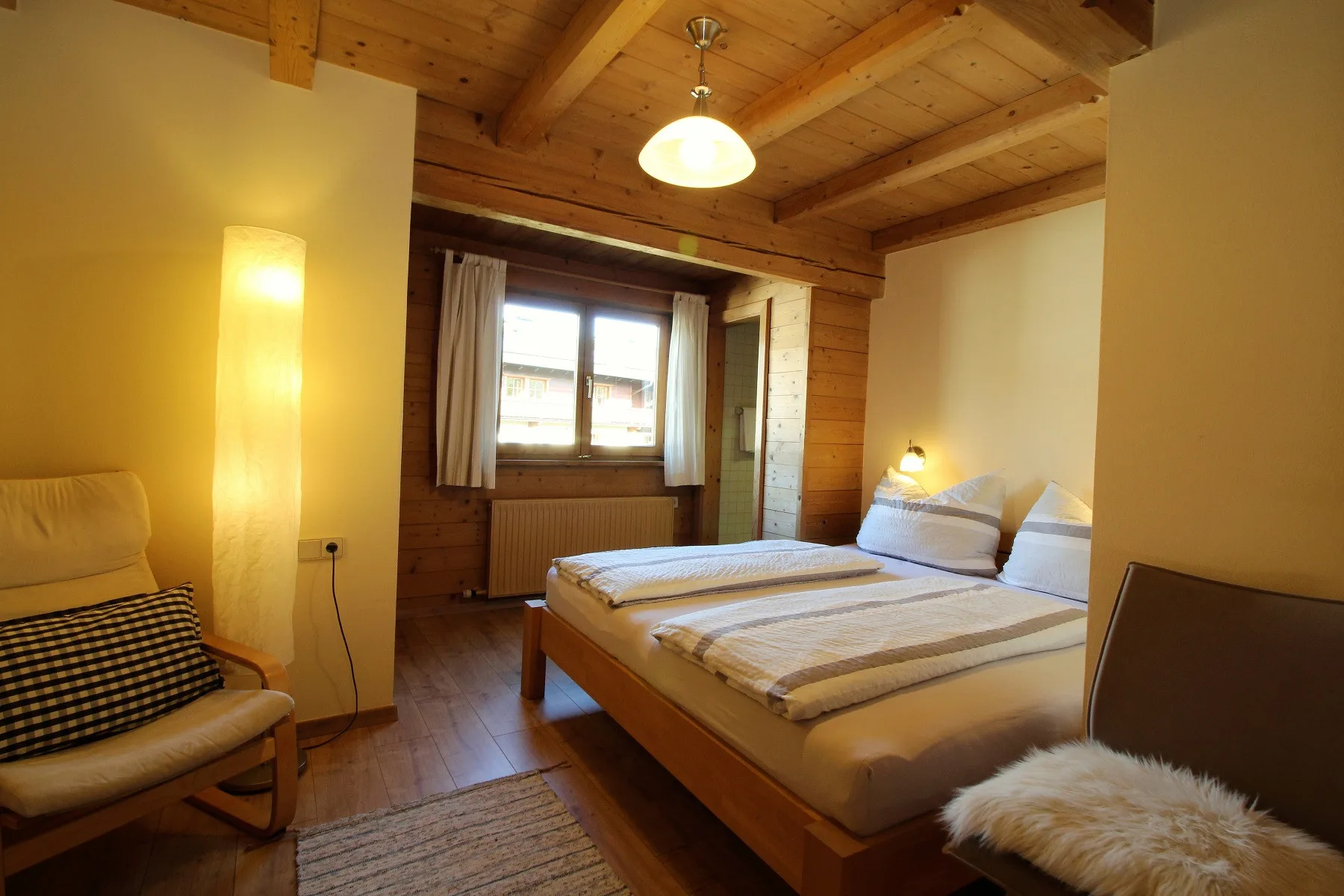 A bedroom with a double bed, a window, and exposed wooden ceiling beams.