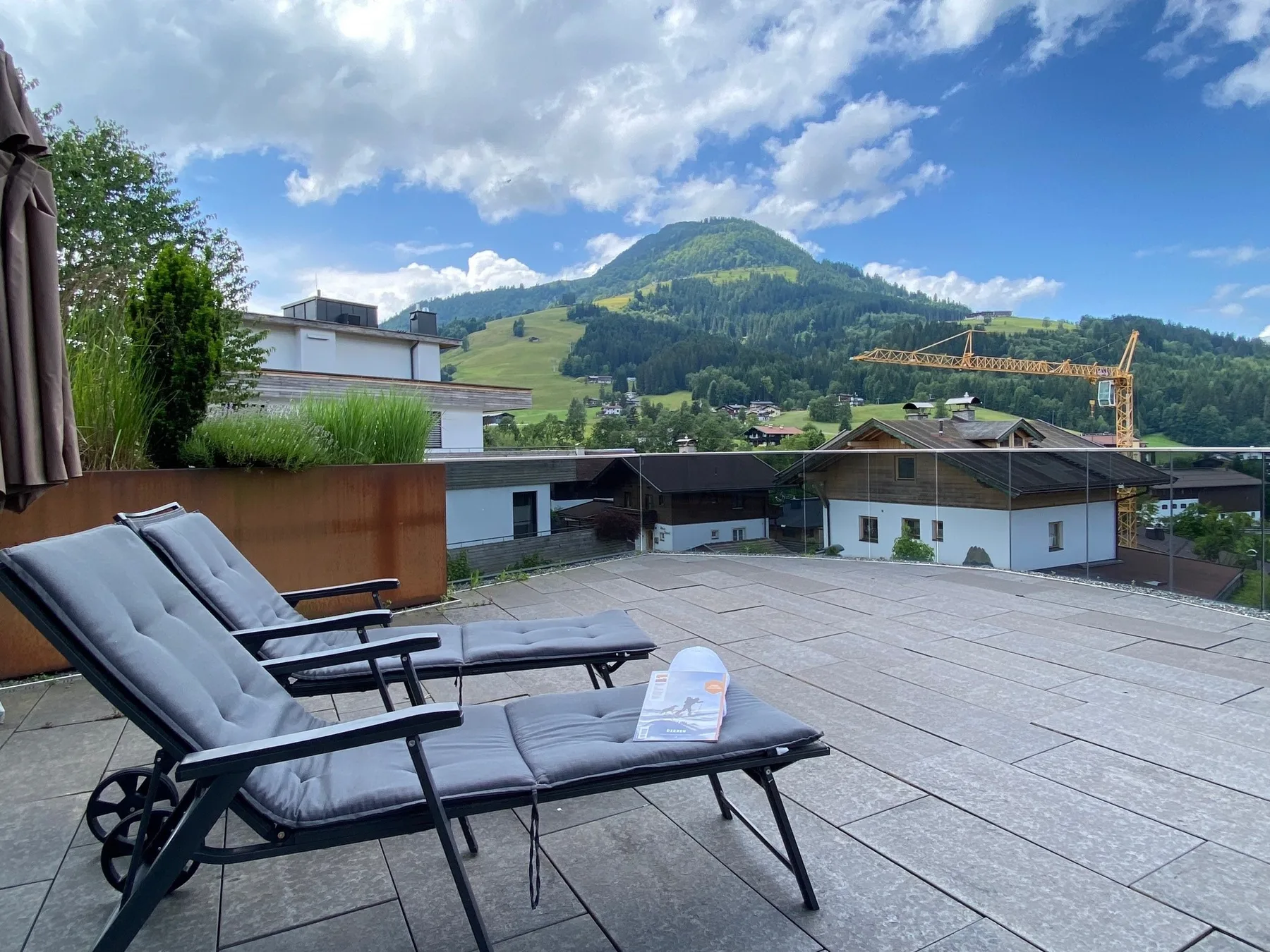 A rooftop terrace with cushioned lounge seating overlooks a green mountain.