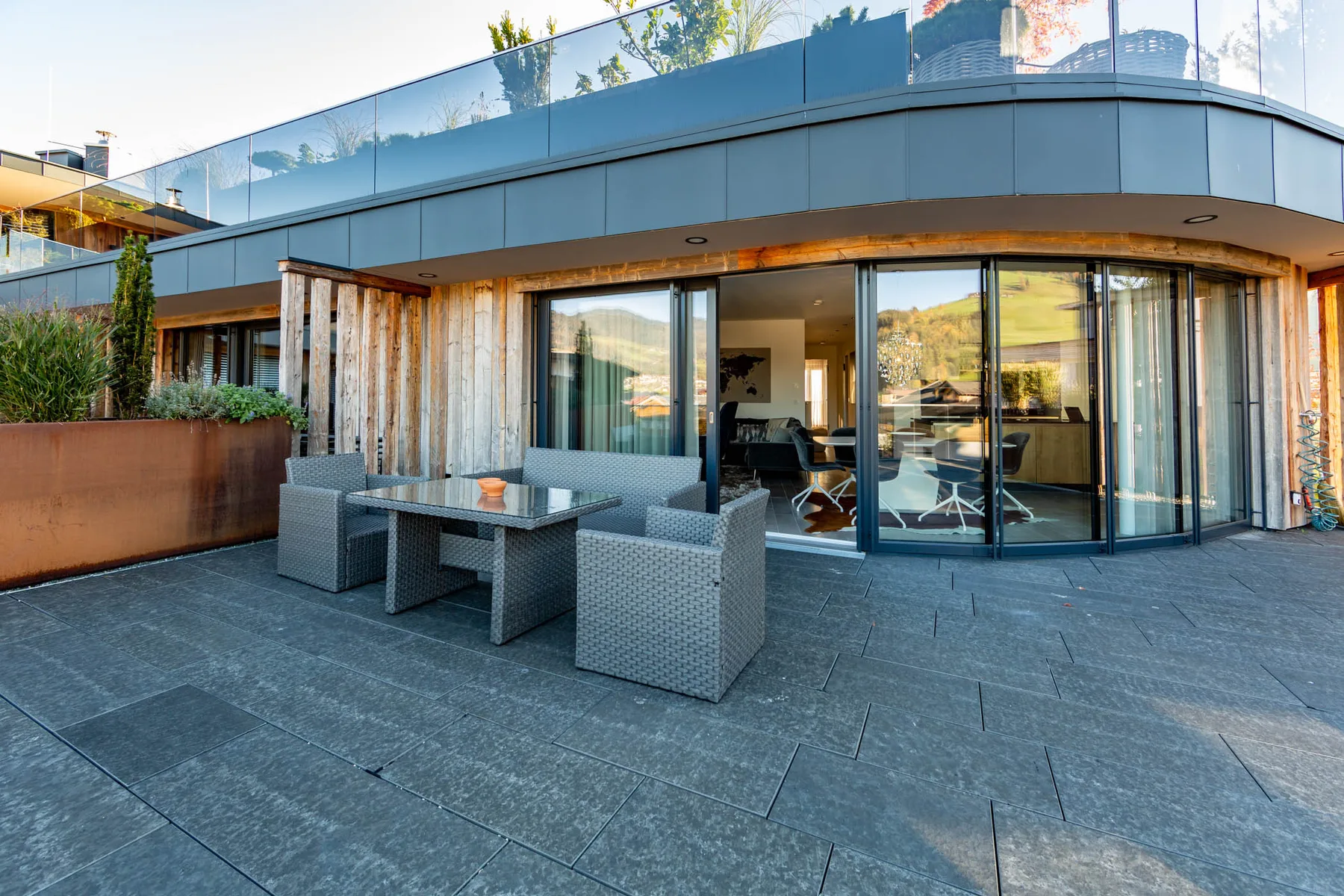 A paved outdoor terrace with woven seating beside large glass doors.