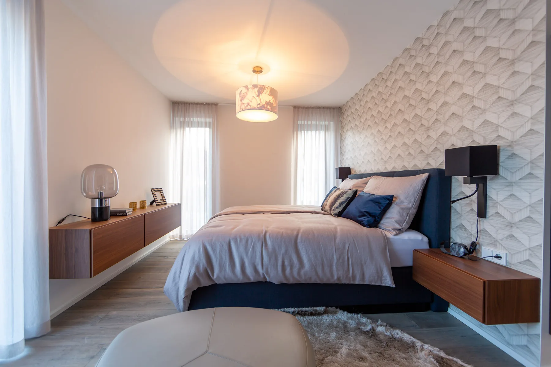 A bedroom with a neatly made bed, bedside tables, and patterned wall decor.