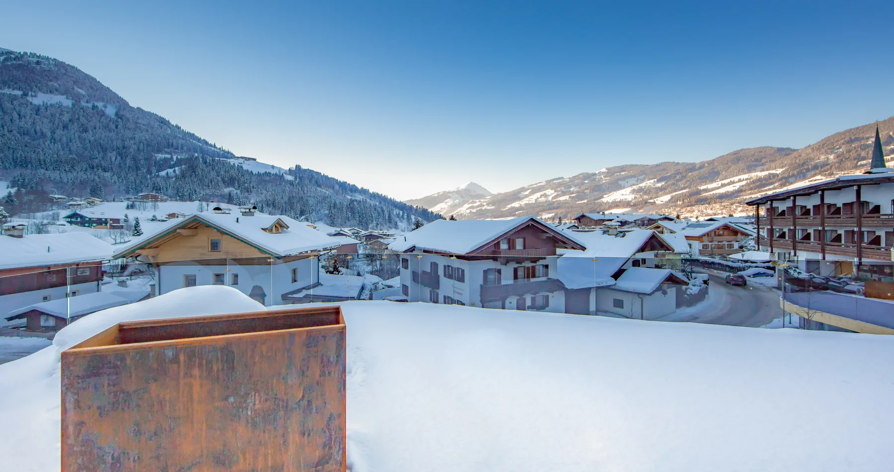 A snow-covered alpine village sits beneath mountain slopes and a clear blue sky.