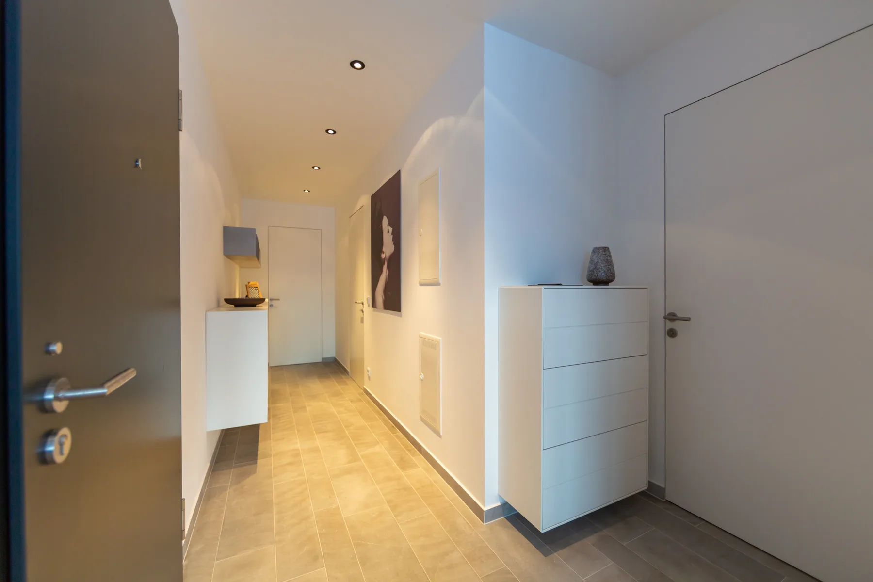 A bright hallway with tiled flooring, wall art, and a white chest of drawers.