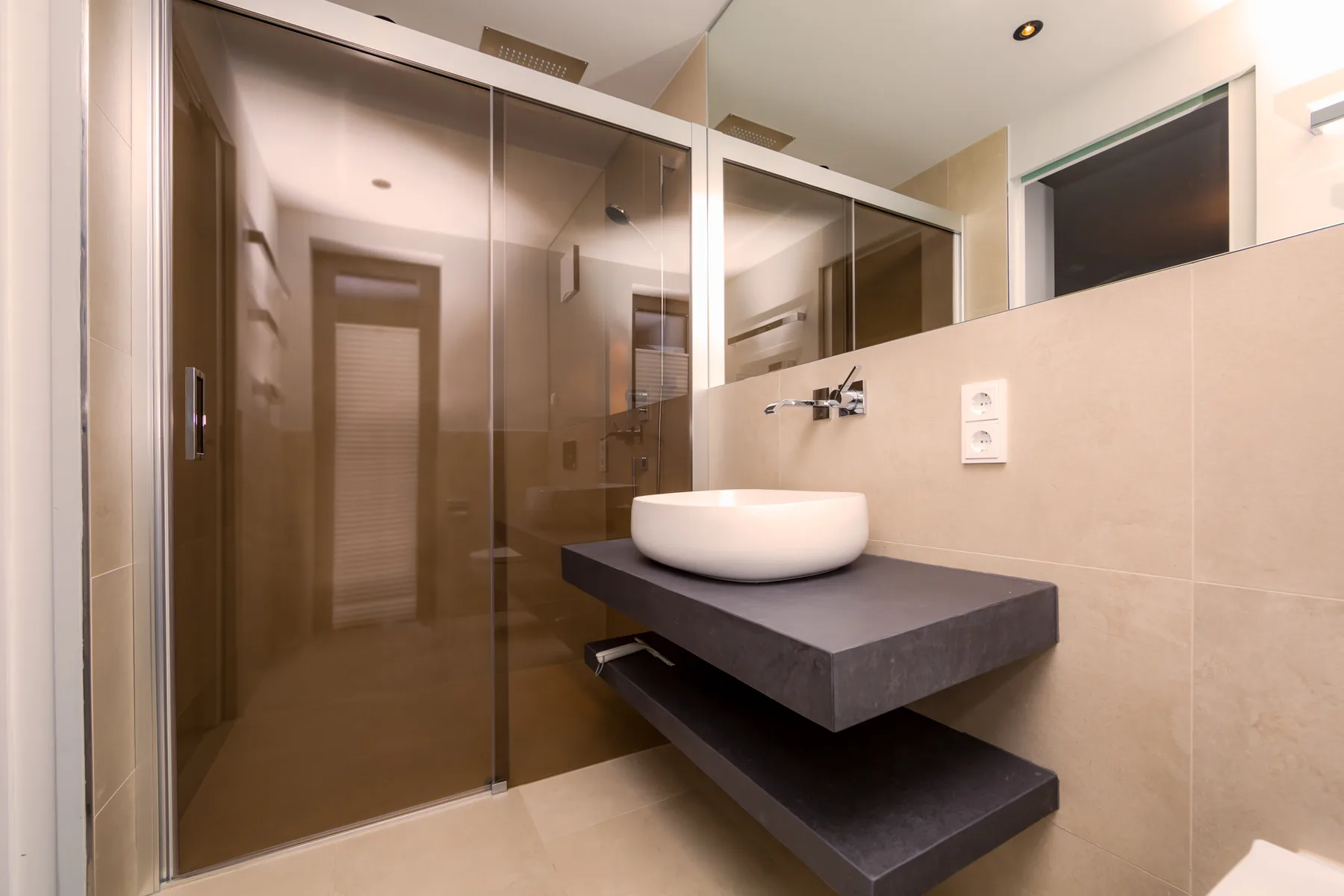 A modern bathroom with a glass shower enclosure and a vessel sink on a dark vanity.