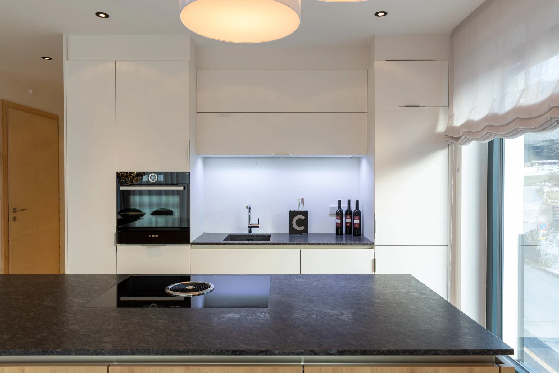 A modern kitchen with white cabinets and a dark countertop.