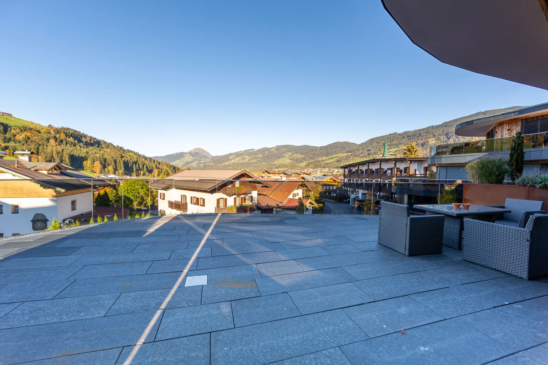 A broad outdoor terrace overlooks buildings and green hills beneath a clear sky.