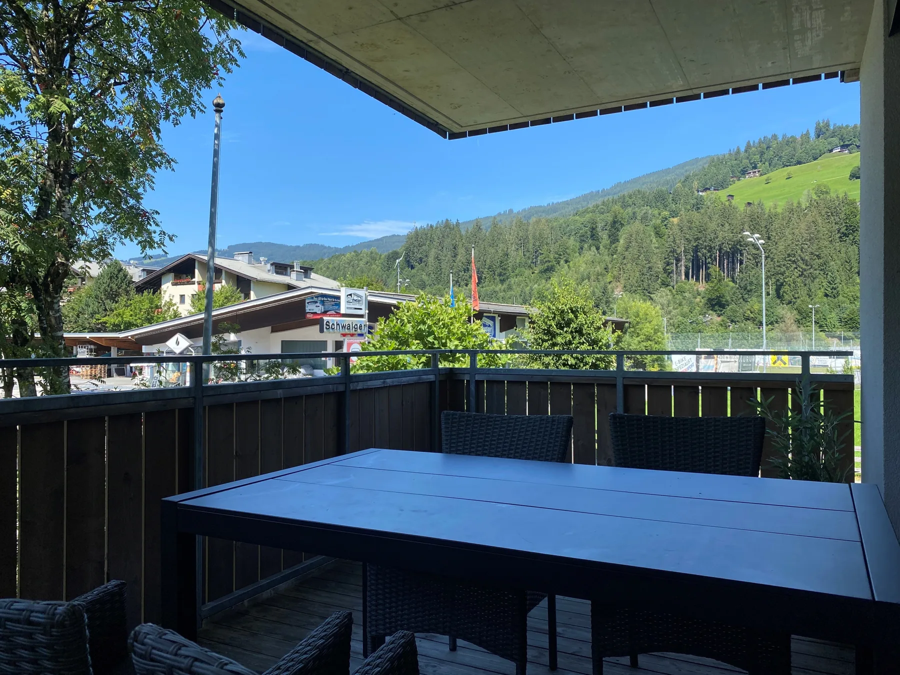 A covered outdoor dining area overlooks green hills and nearby buildings.