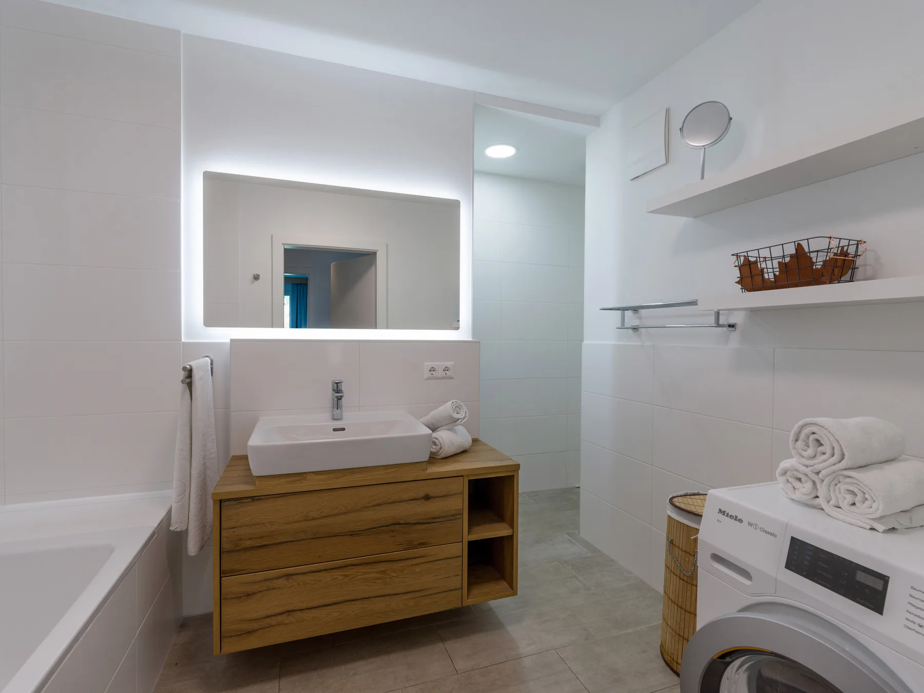 A bright bathroom with a wooden vanity, mirror, and washing machine.