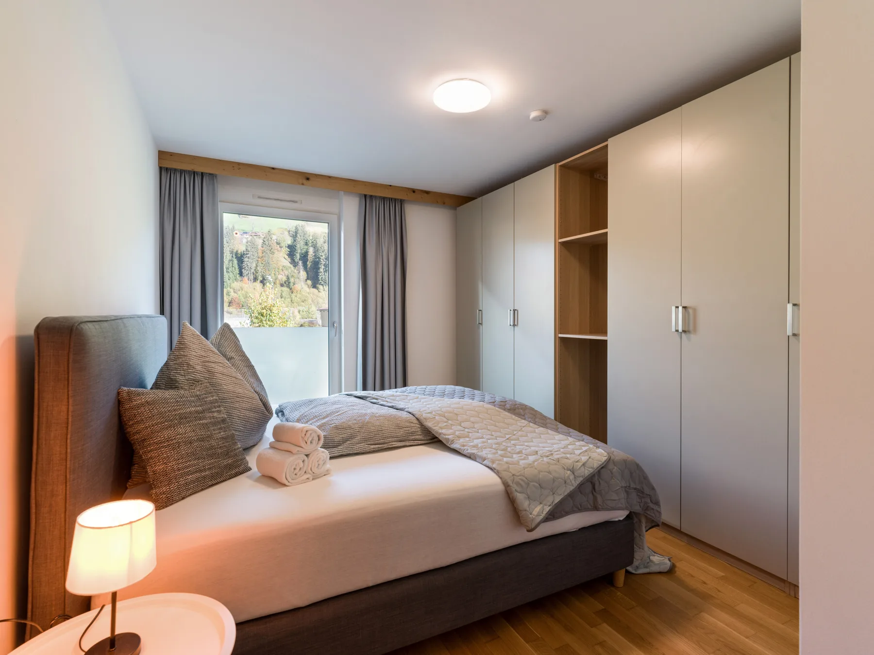 A bedroom with a bed beside built-in wardrobes and a window.