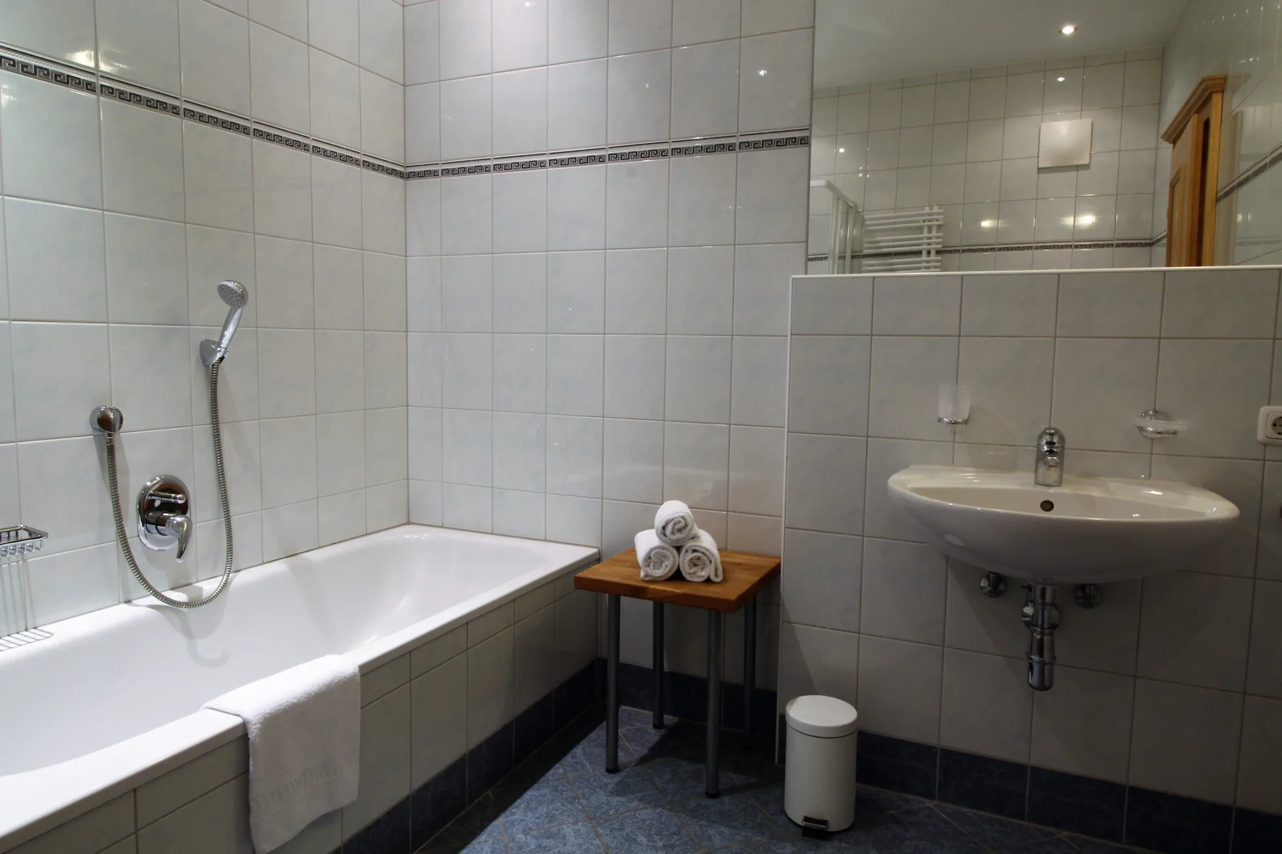 A tiled bathroom with a bathtub, shower, and wall-mounted sink.