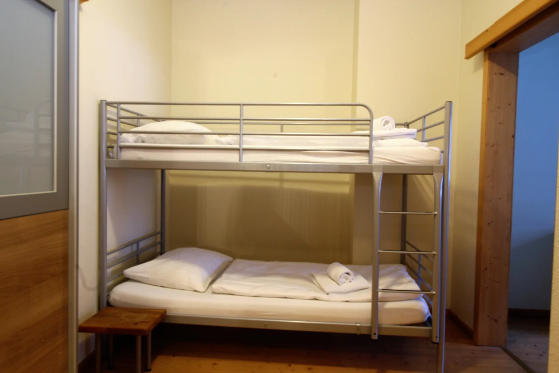 A bunk bed with white bedding stands in a small bedroom.