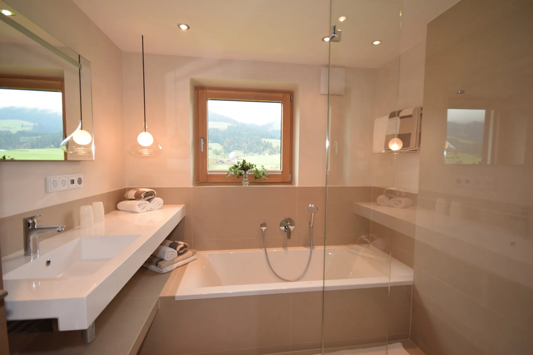 Un baño luminoso con una bañera bajo una ventana con vistas a colinas verdes.