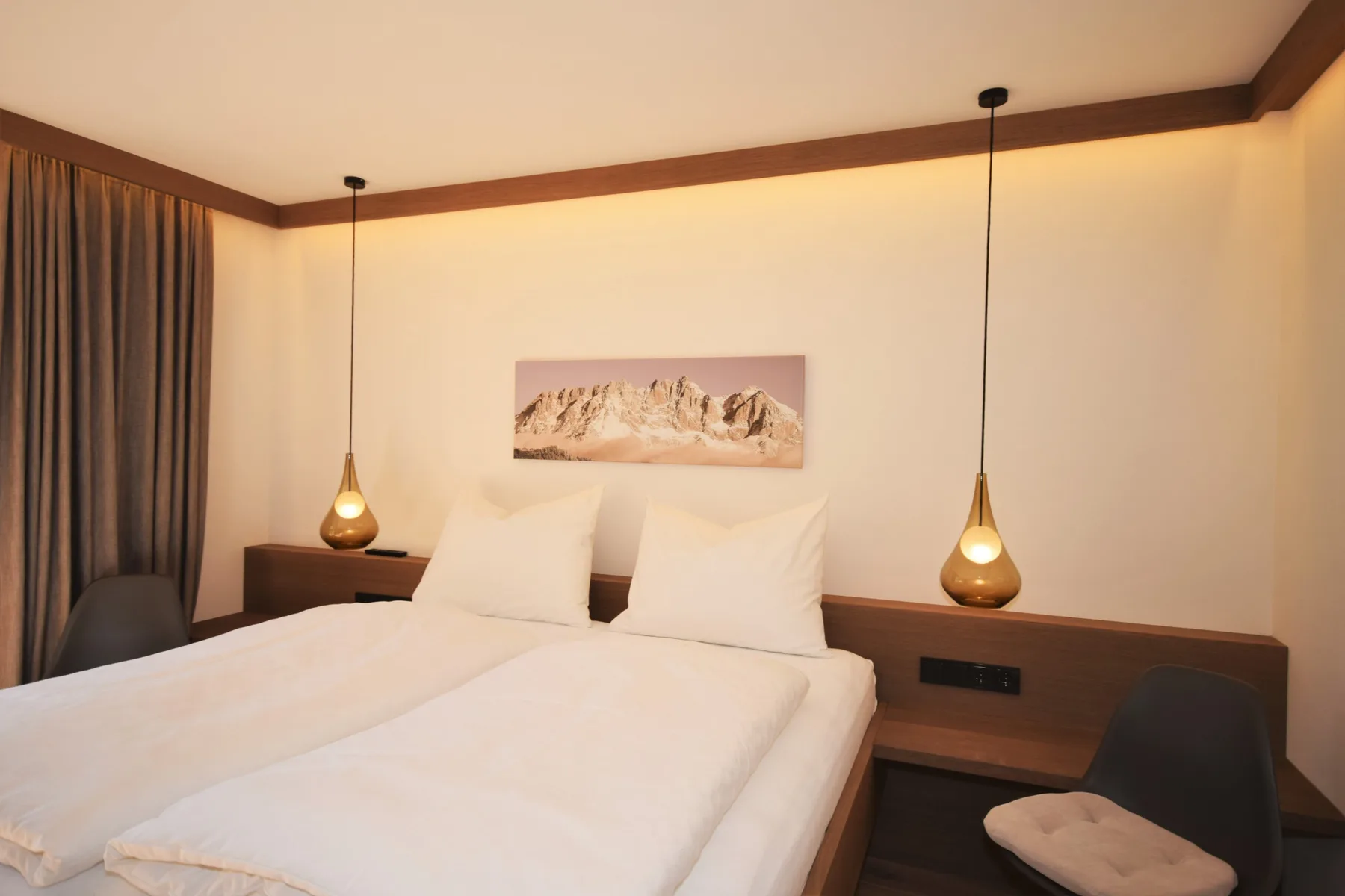 Un dormitorio con una cama bien arreglada y lámparas colgantes junto al cabecero.