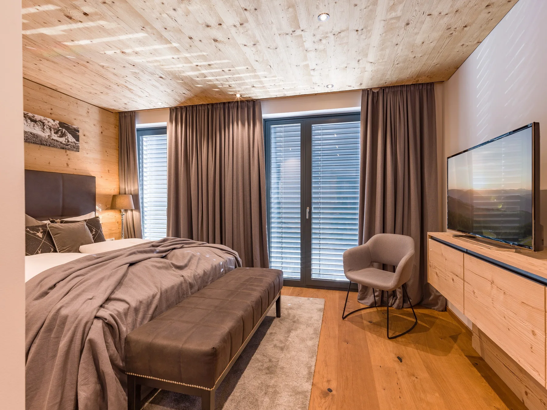 Un dormitorio con una cama, cortinas largas y un televisor.